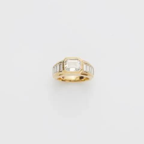 An 18k yellow gold diamond band ring with an emerald-cut diamond solitaire.