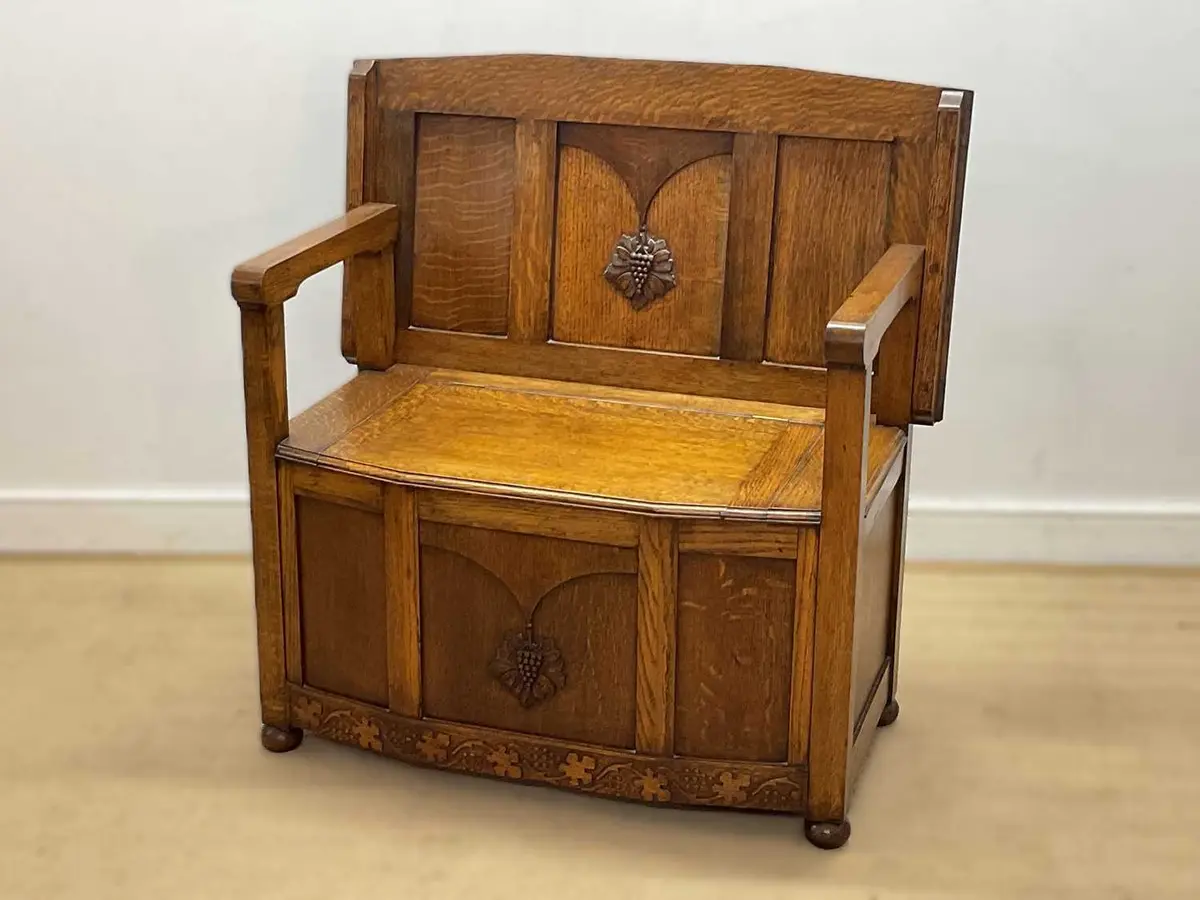 An oak monk's bench with storage beneath and engraved with grapes and vines