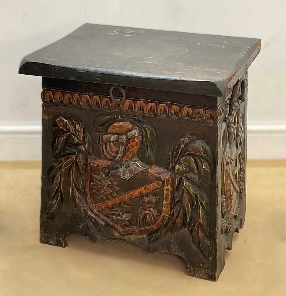 A stained wooden coal box with carved coat of arms to the front