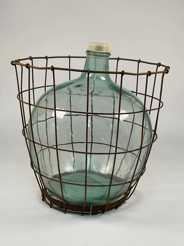 A vintage green glass carboy enclosed within a metal wire cage