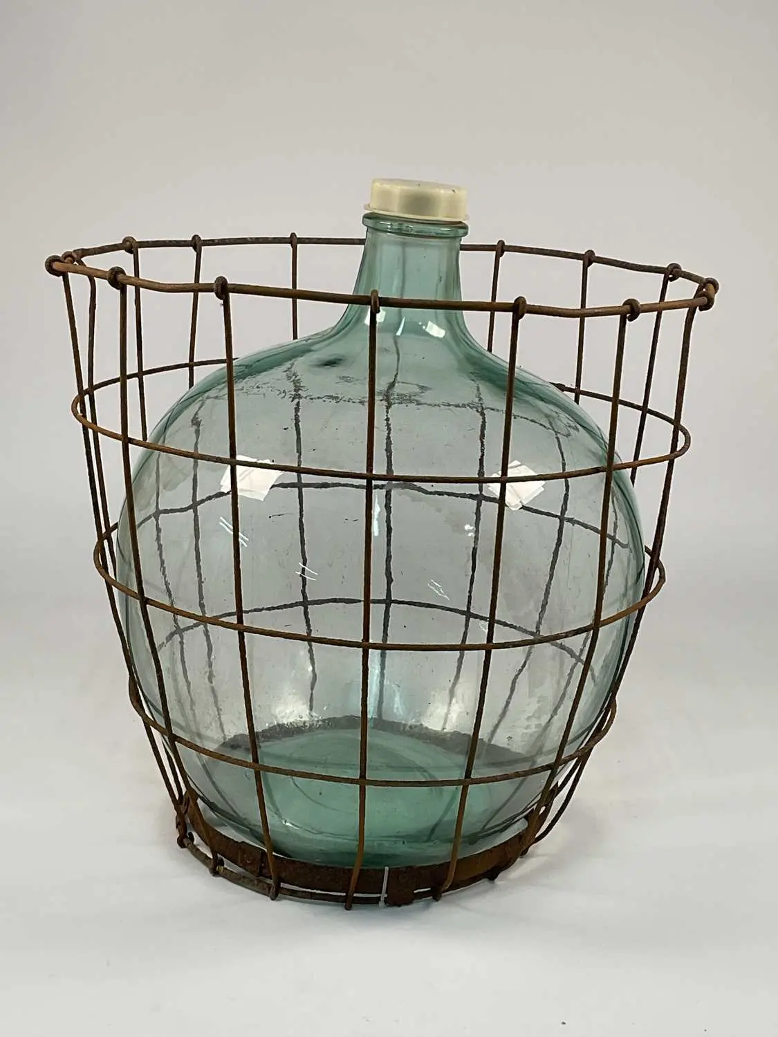A vintage green glass carboy enclosed within a metal wire cage
