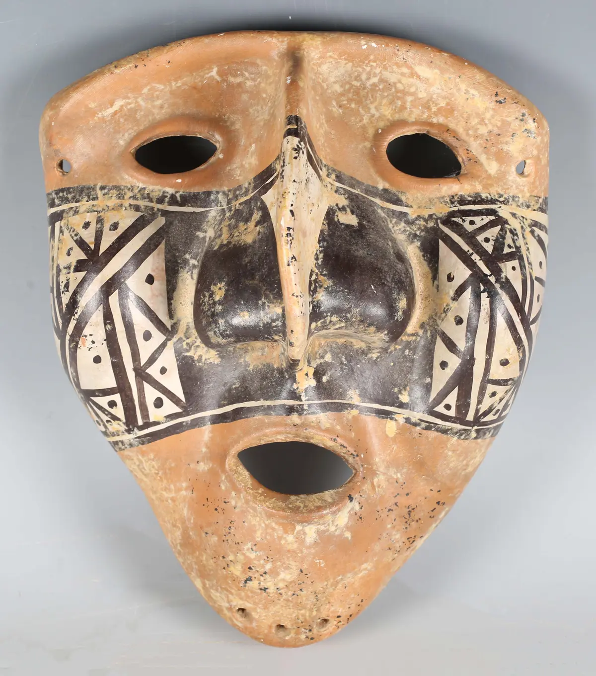 A pre-Columbian style terracotta mask, painted with a band of geometric