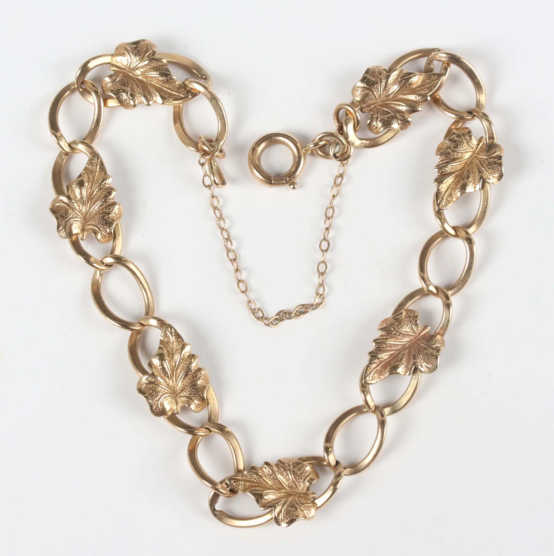 A 9ct gold curblink bracelet, applied with leaf motifs at intervals