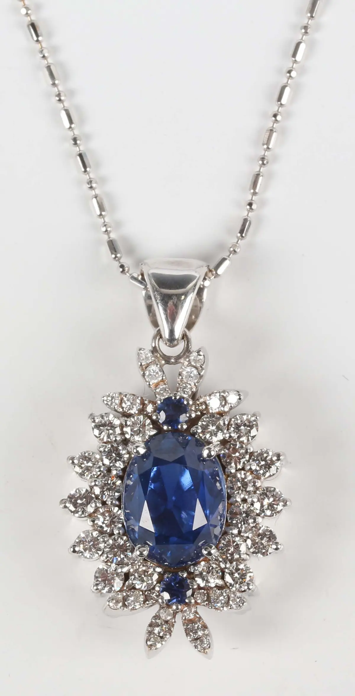 A white gold, sapphire and diamond cluster pendant, claw set with