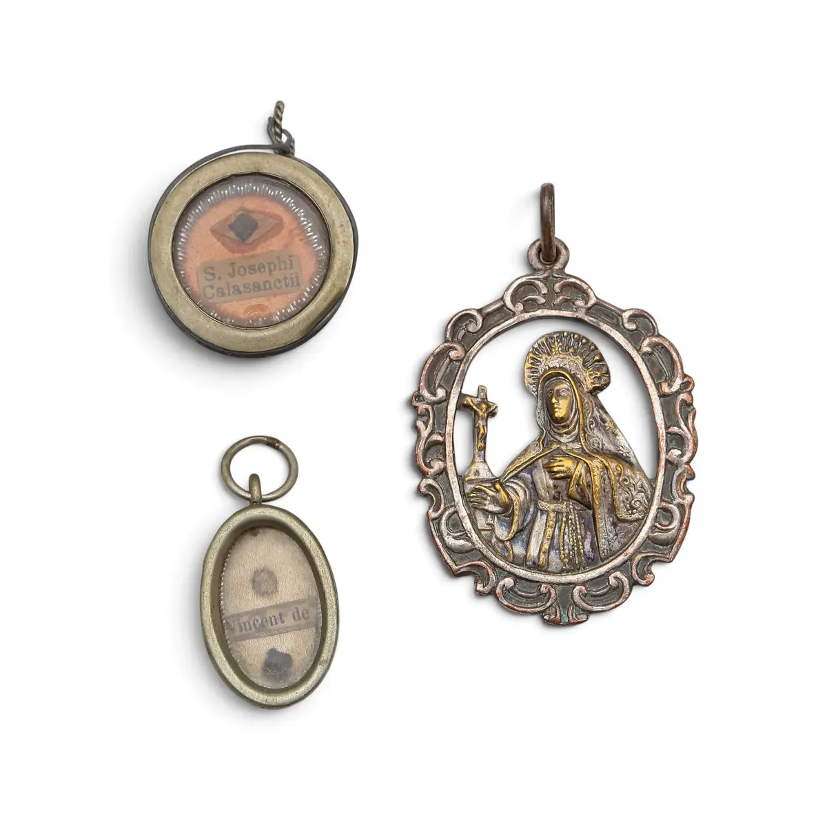 Two reliquary pendants and a Saint Teresa medal in silvery metal, 19th Century.