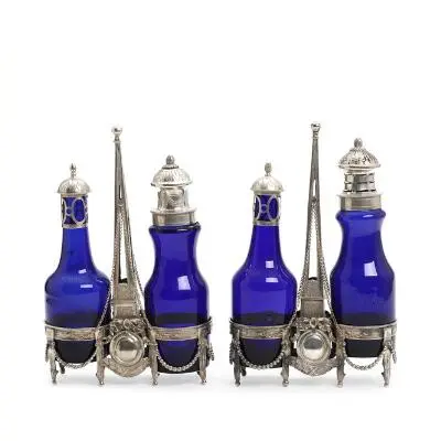 A pair of silver oil and vinegar sets, each with two blue glass bottles.