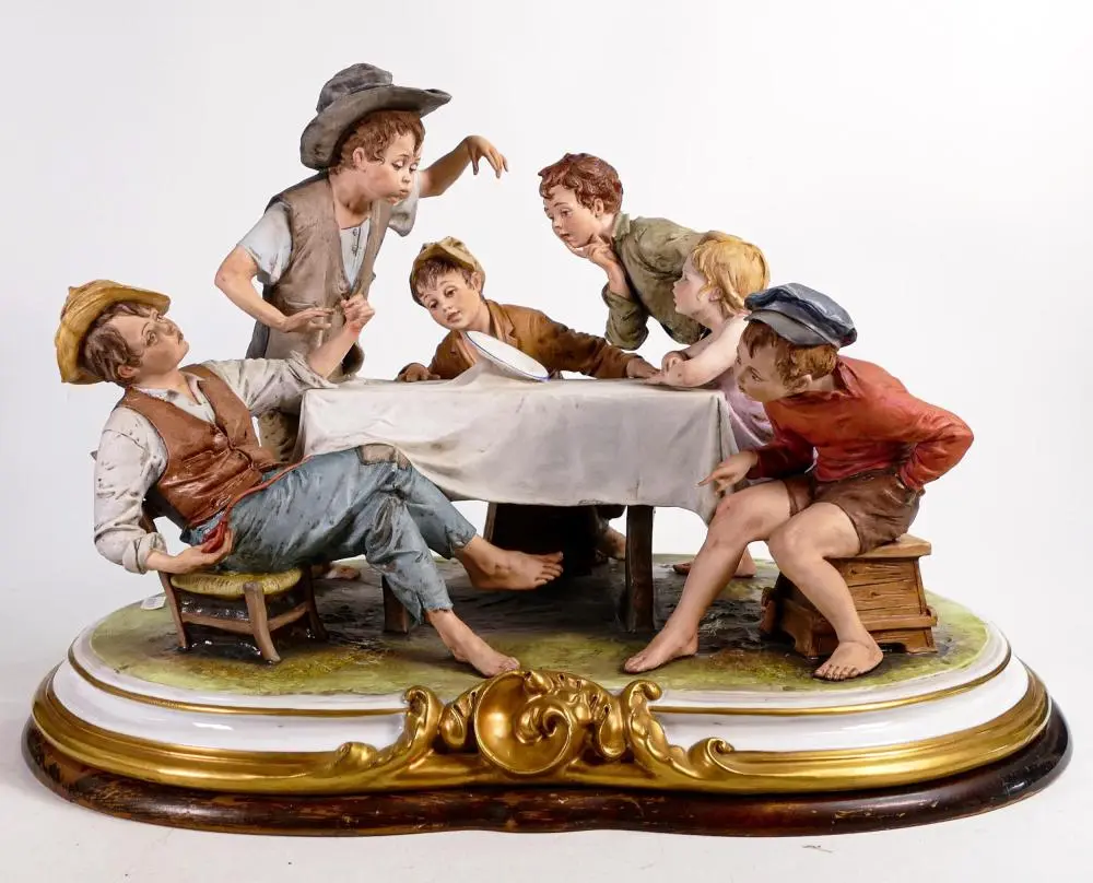 A large Capodimonte group of 6 children sitting around a table watching a m